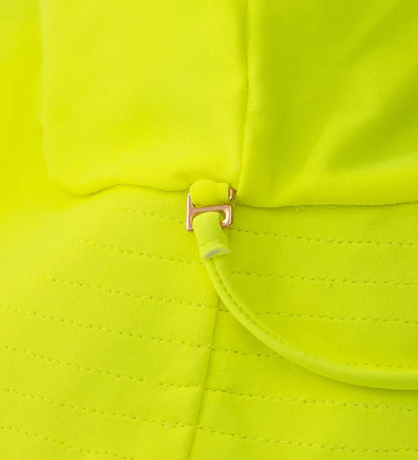 Close-up of a bright neon yellow-green fabric garment with a small metallic gold zipper pull and matching fabric tab detail.