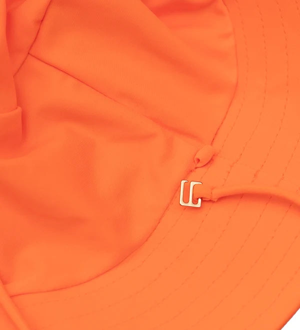 Close-up of a bright orange fabric product, likely a hat or sun hat brim, featuring a small metallic silver U-shaped hardware detail near the center.