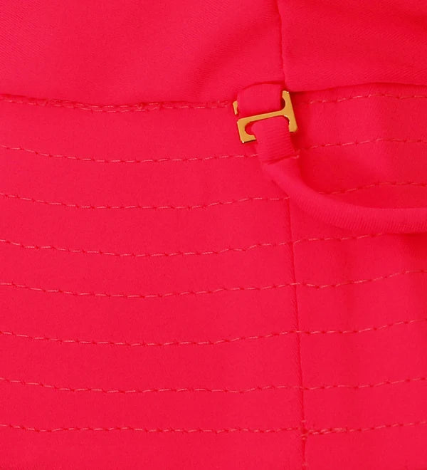 Close-up of a bright pink fabric product with horizontal stitching and a small gold metal buckle detail.