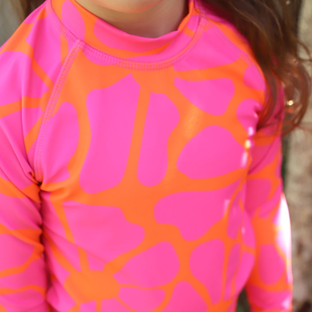 Close-up of a child wearing a long-sleeve rashie with a bold pink and orange abstract pattern from Vizzies Swim.