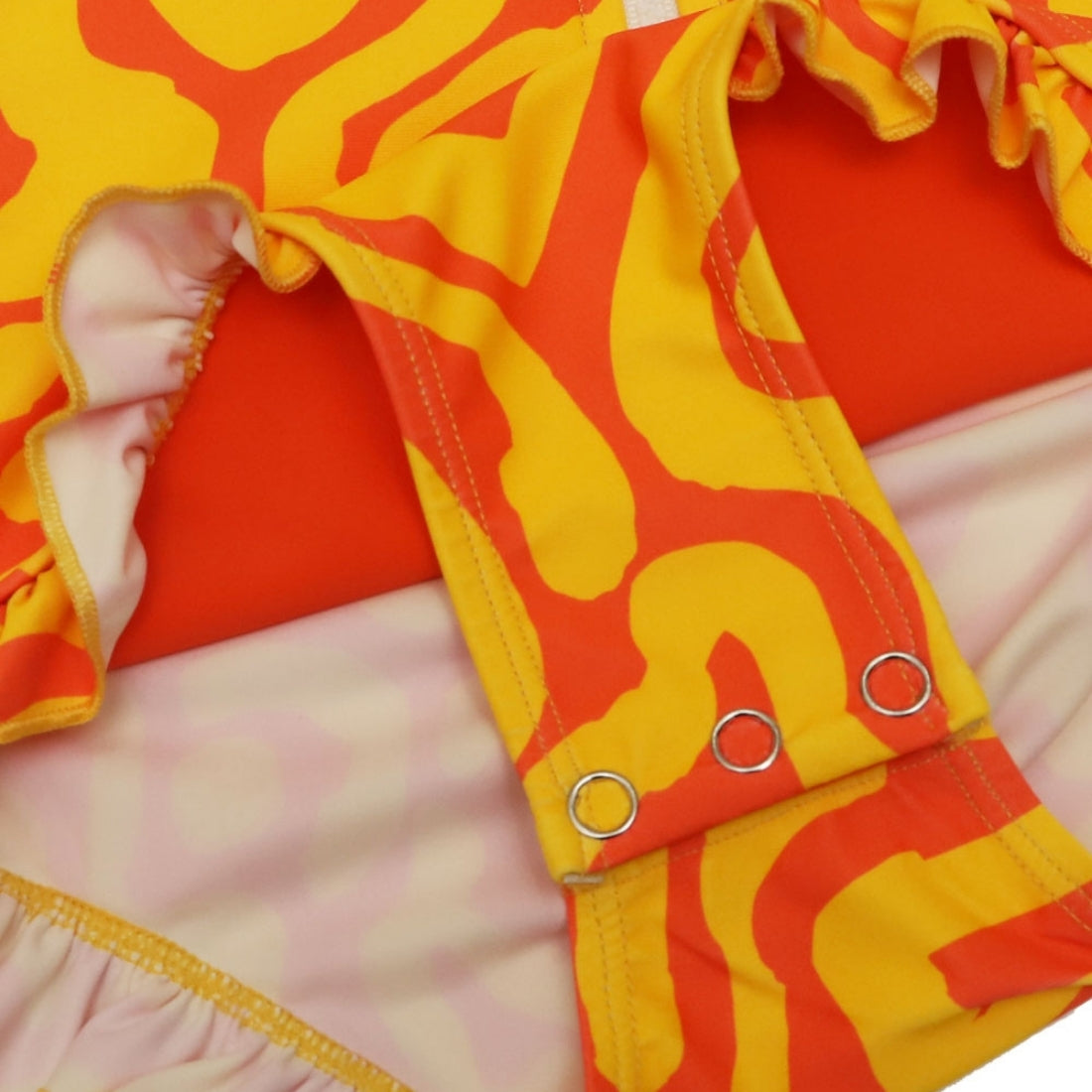 Close-up of a Vizzies Swim girls one-piece frill swimsuit in bright sunburst pattern, showing the crotch snaps and ruffle details. 