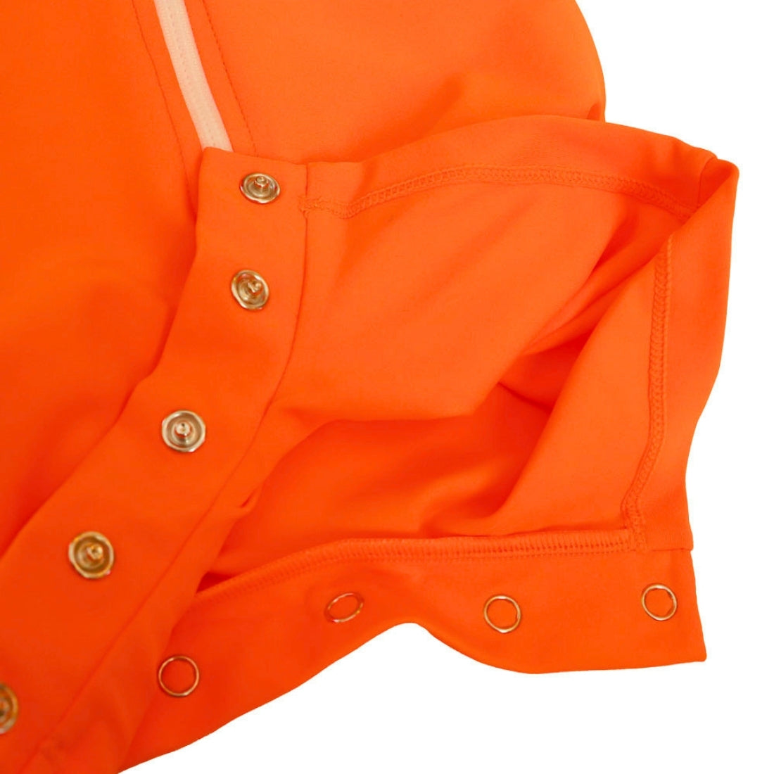 Close-up detail of an orange baby swimsuit, showing the crotch with three metal grommets and a light-colored zipper tab on a white background.